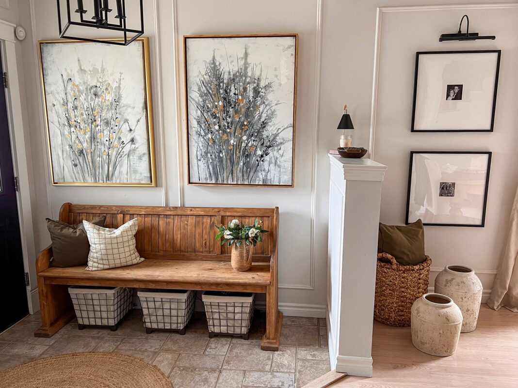 wooden church pew style bench in entryway with two large paintings above to illustrate decorating style